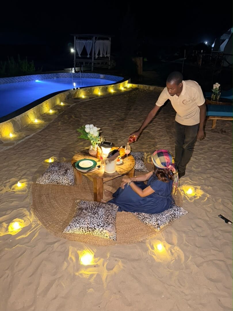 A private dinner laid on the sand beside the lit pool at Cterra Saadani, at night