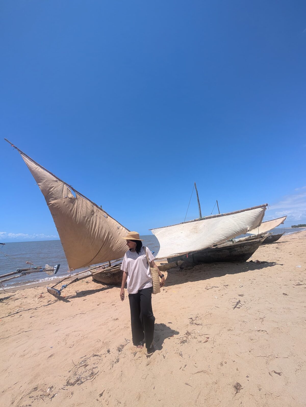 A dhow with its sail raised on the sand, the Indian Ocean behind