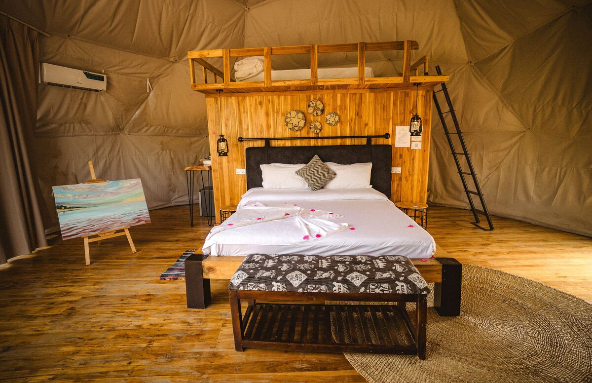 Inside a Family Garden dome at Cterra Saadani, with the loft rail and the bench at the foot of the bed