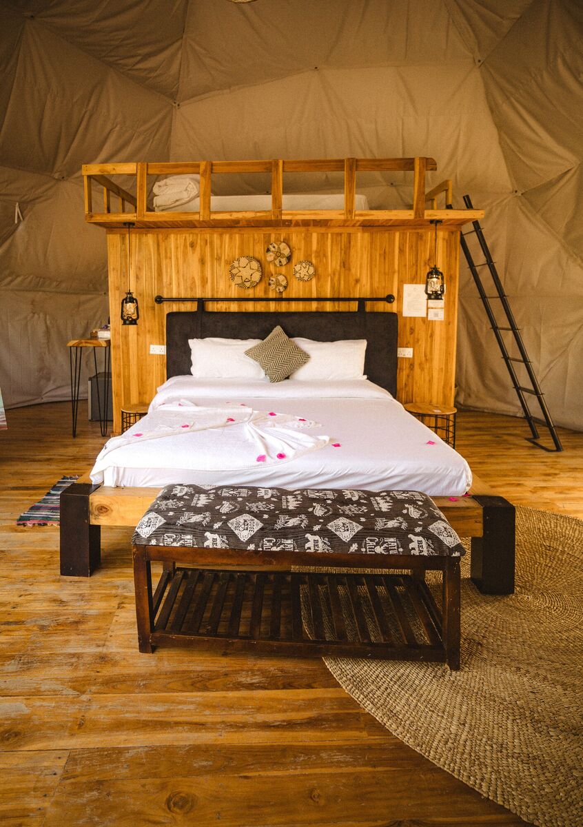 Inside a Family Garden dome at Cterra Saadani, with the loft rail and the bench at the foot of the bed