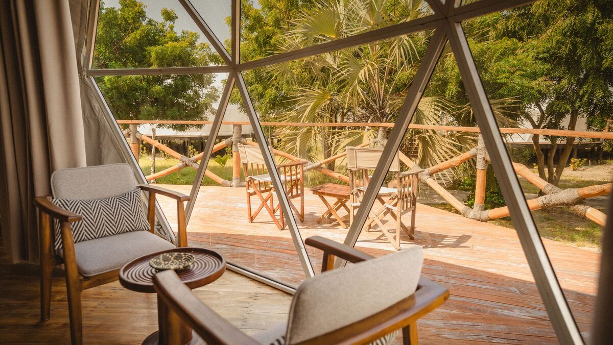 Inside a Family Garden dome at Cterra Saadani, with the loft rail and the bench at the foot of the bed