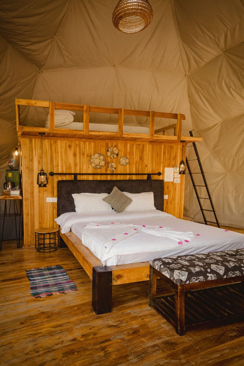 Inside a Family Garden dome at Cterra Saadani, with the loft rail and the bench at the foot of the bed