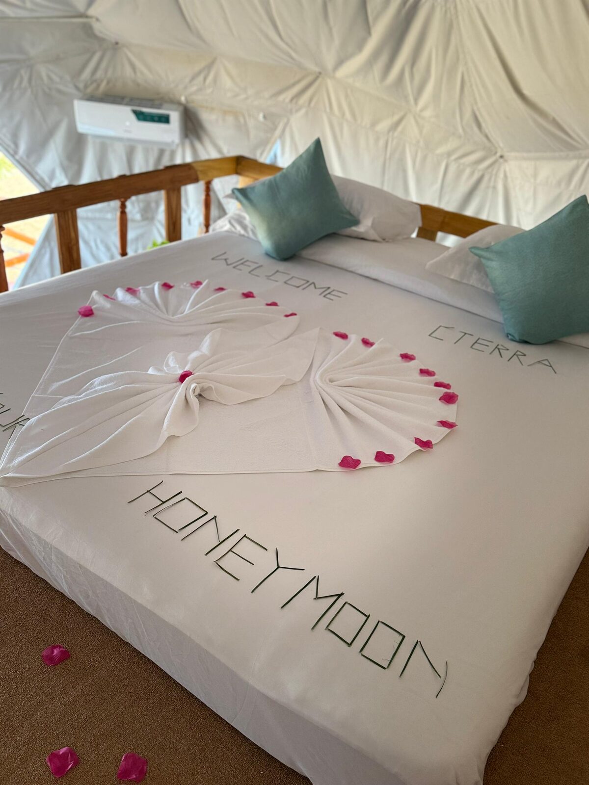 A honeymoon setup: towel swans, rose petals and «HONEYMOON» laid on the bed