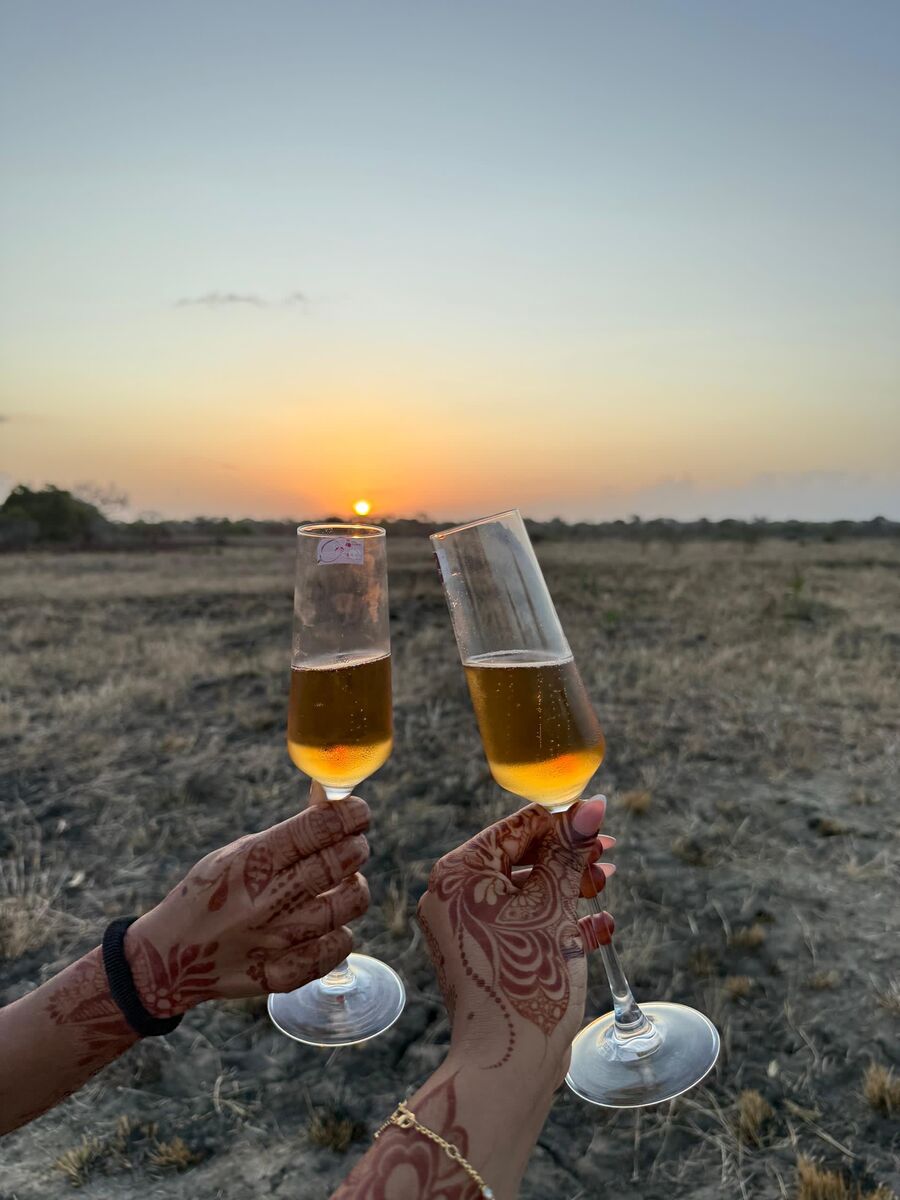Two guests with henna-painted hands raising glasses against the setting sun over Saadani