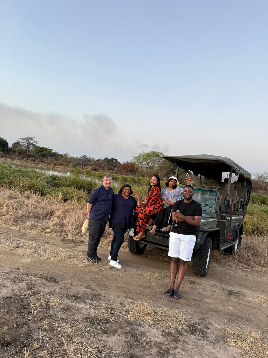 Guests with drinks beside the safari vehicle on the salt pan at Cterra Saadani, at sunset