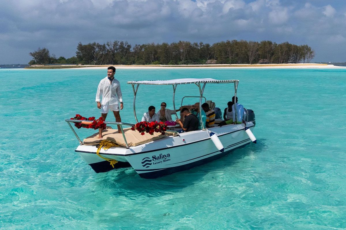 The private boat moored off a sandbank in clear turquoise water, guests aboard under the canopy