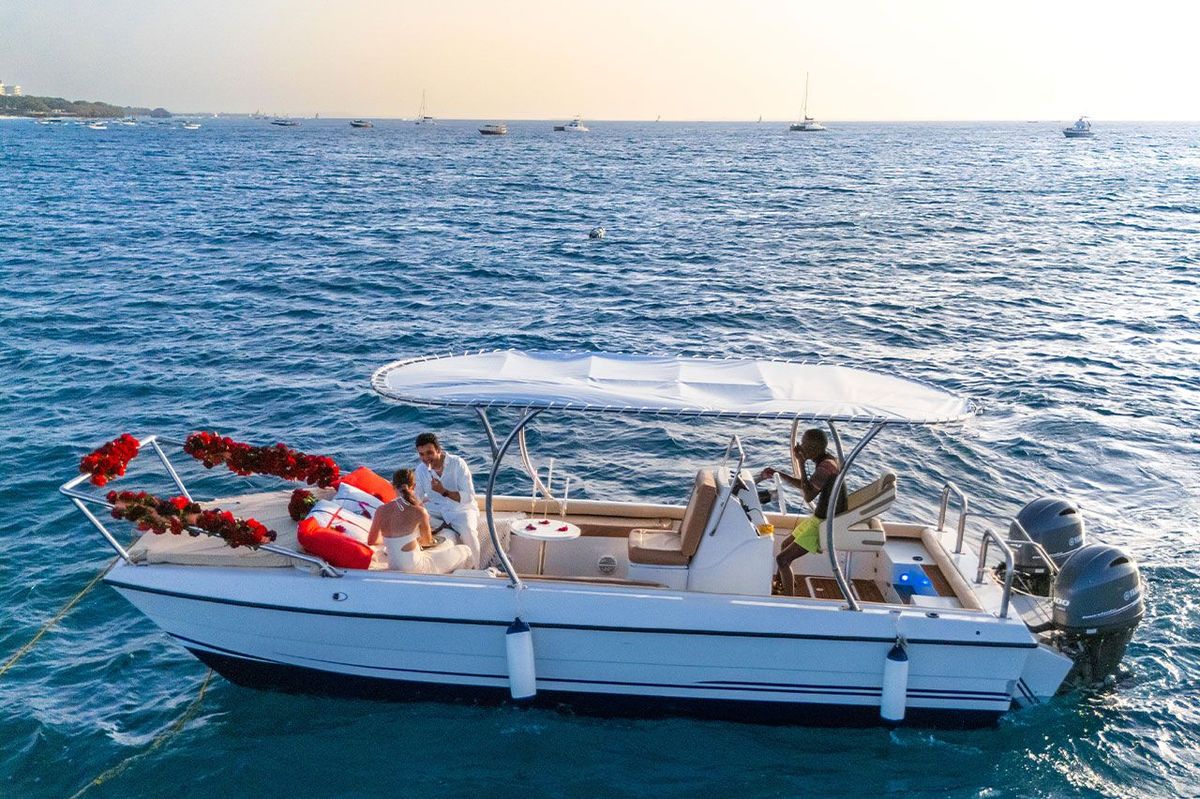 The private boat seen from the side on bright turquoise water, guests under the canopy