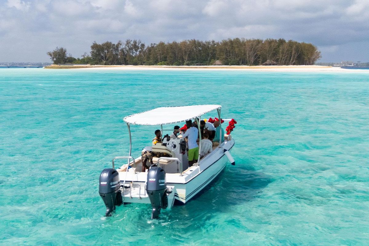 The boat at anchor over pale sand, a wooded sandbank on the horizon